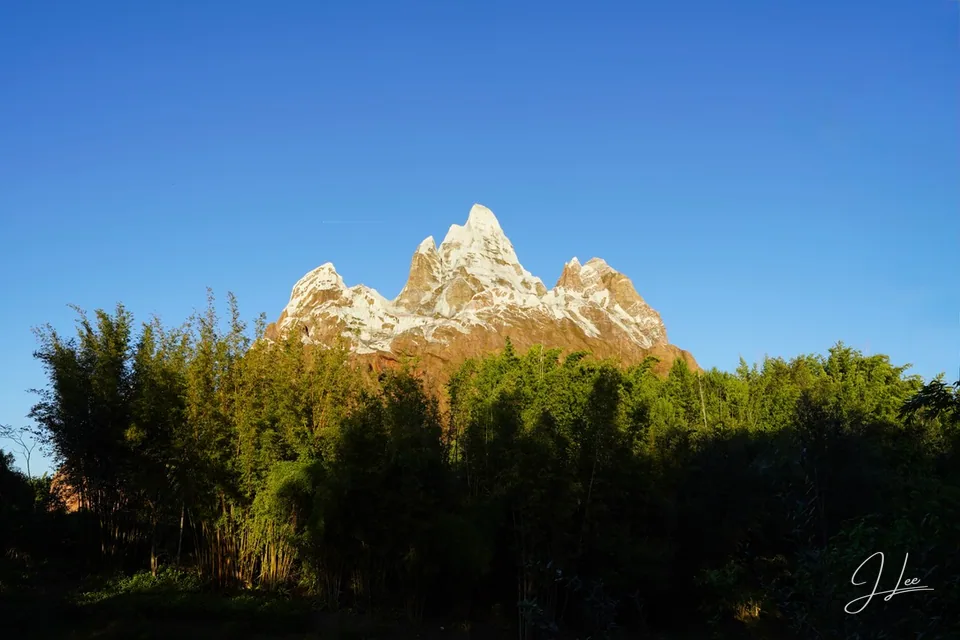 A snow-topped mountain attraction rises above bamboo beneath a clear blue sky.