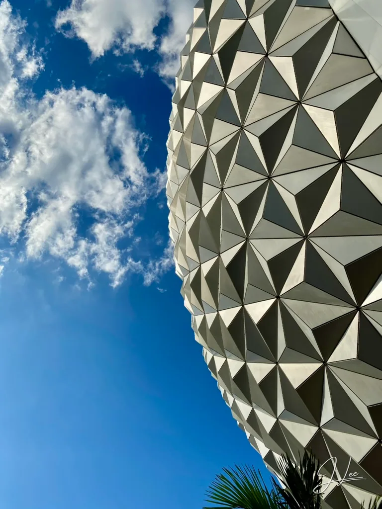 Triangular panels curve along a large sphere beside blue sky and white clouds.